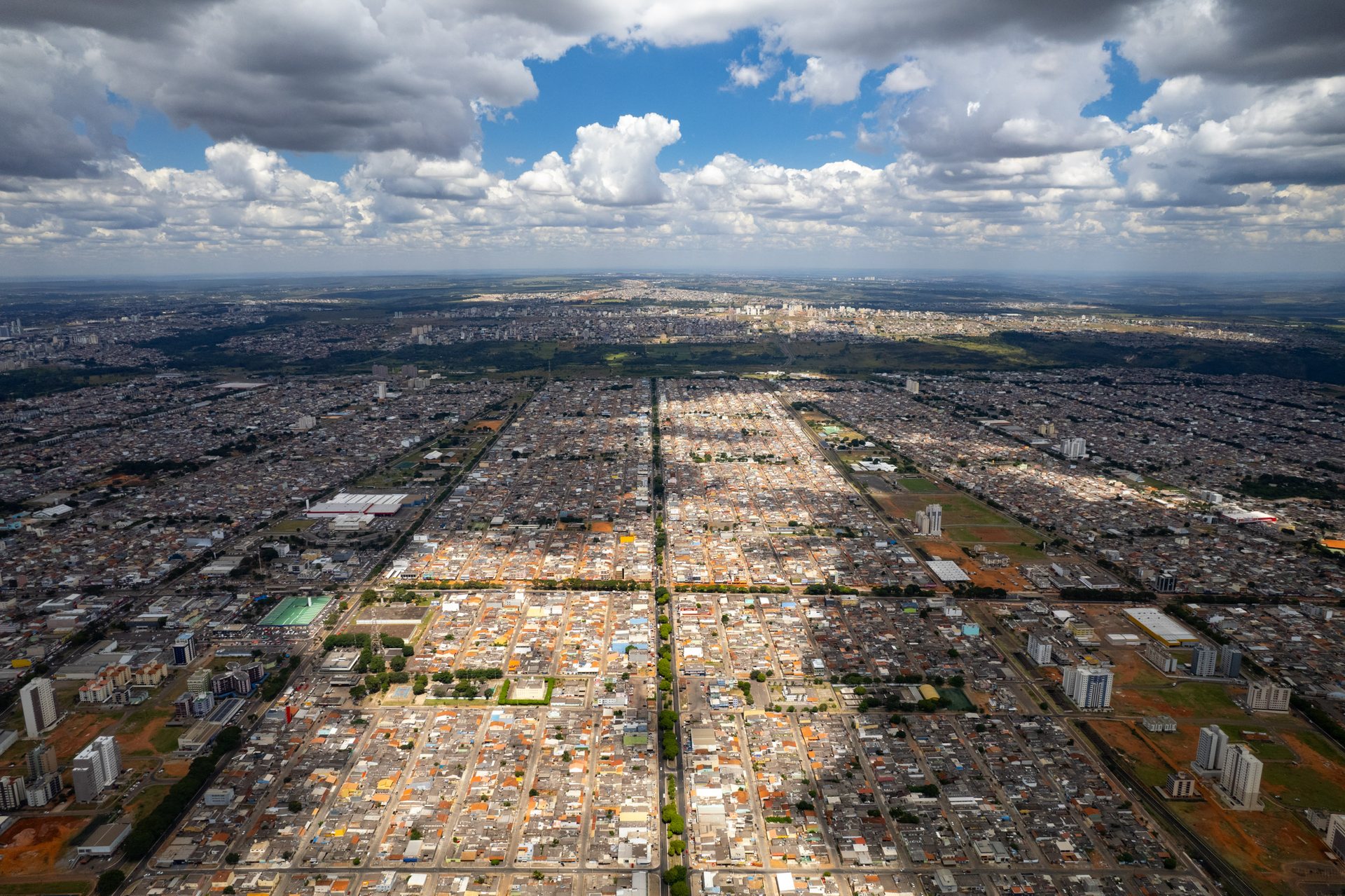 Wide aerial view of Ceilândia, outside Brasília, with a clear central avenue dividing dense residential neighborhoods under a dramatic sky.