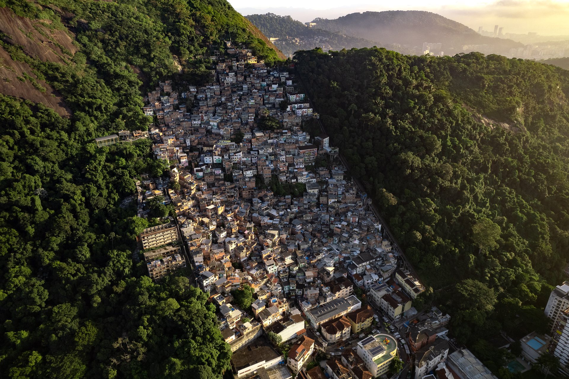 Aerial view of Santa Marta favela in Rio de Janeiro, Brazil, built on a steep hillside surrounded by tropical forest, with dense informal housing cascading down the slope.