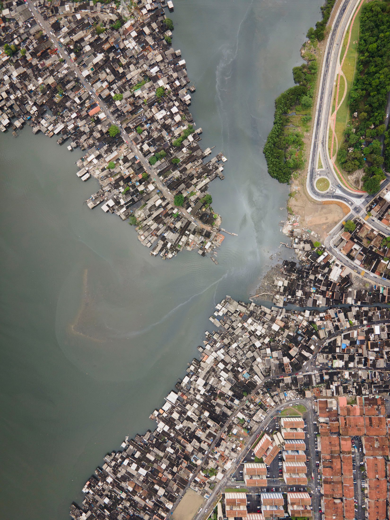 Overhead aerial showing informal stilt homes extending into the water in Santos, next to a road and vegetation.