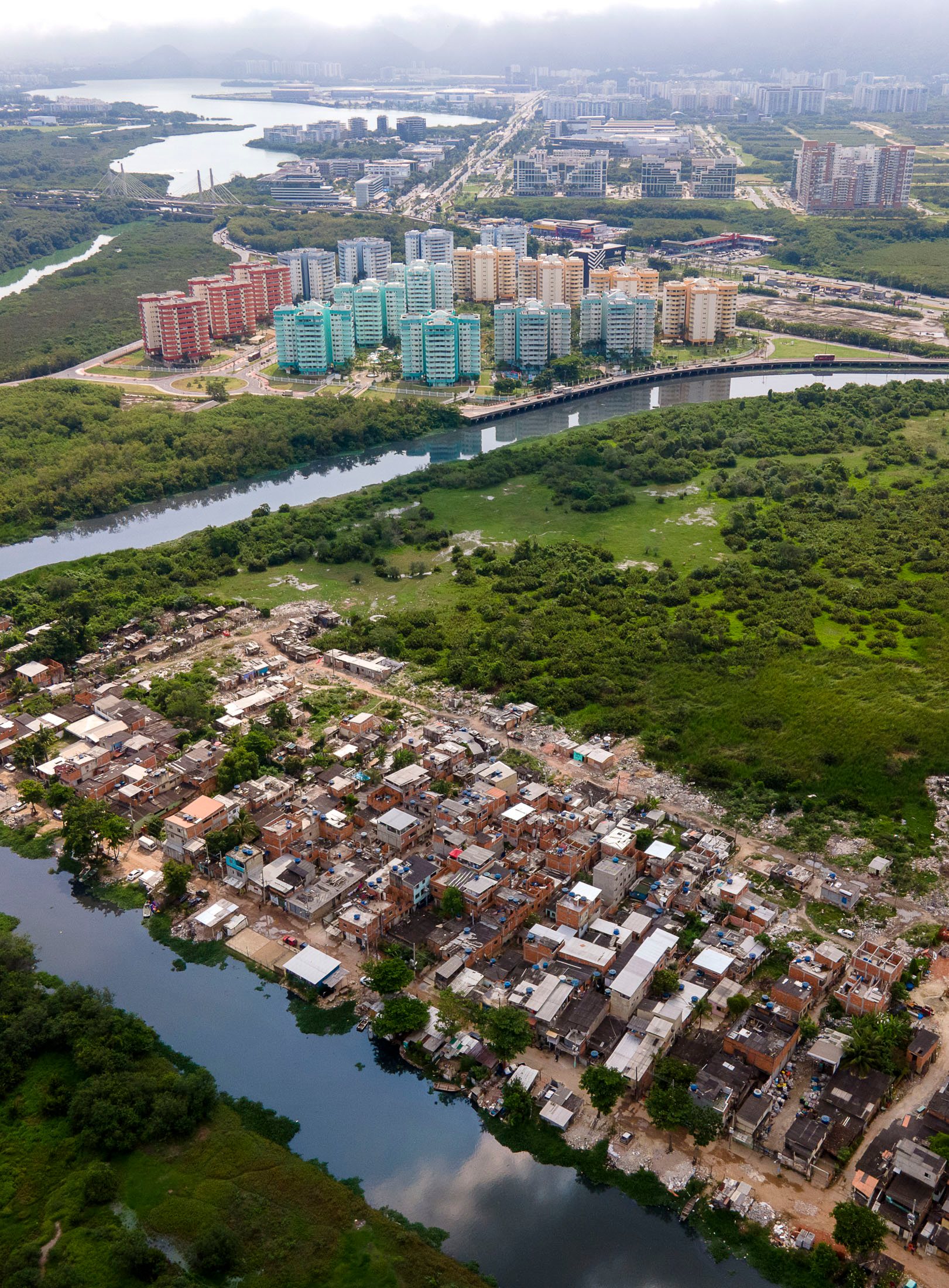 Aerial views of Rio de Janeiro showing stark contrasts between colorful Olympic housing developments and adjacent informal settlements along the lagoon.