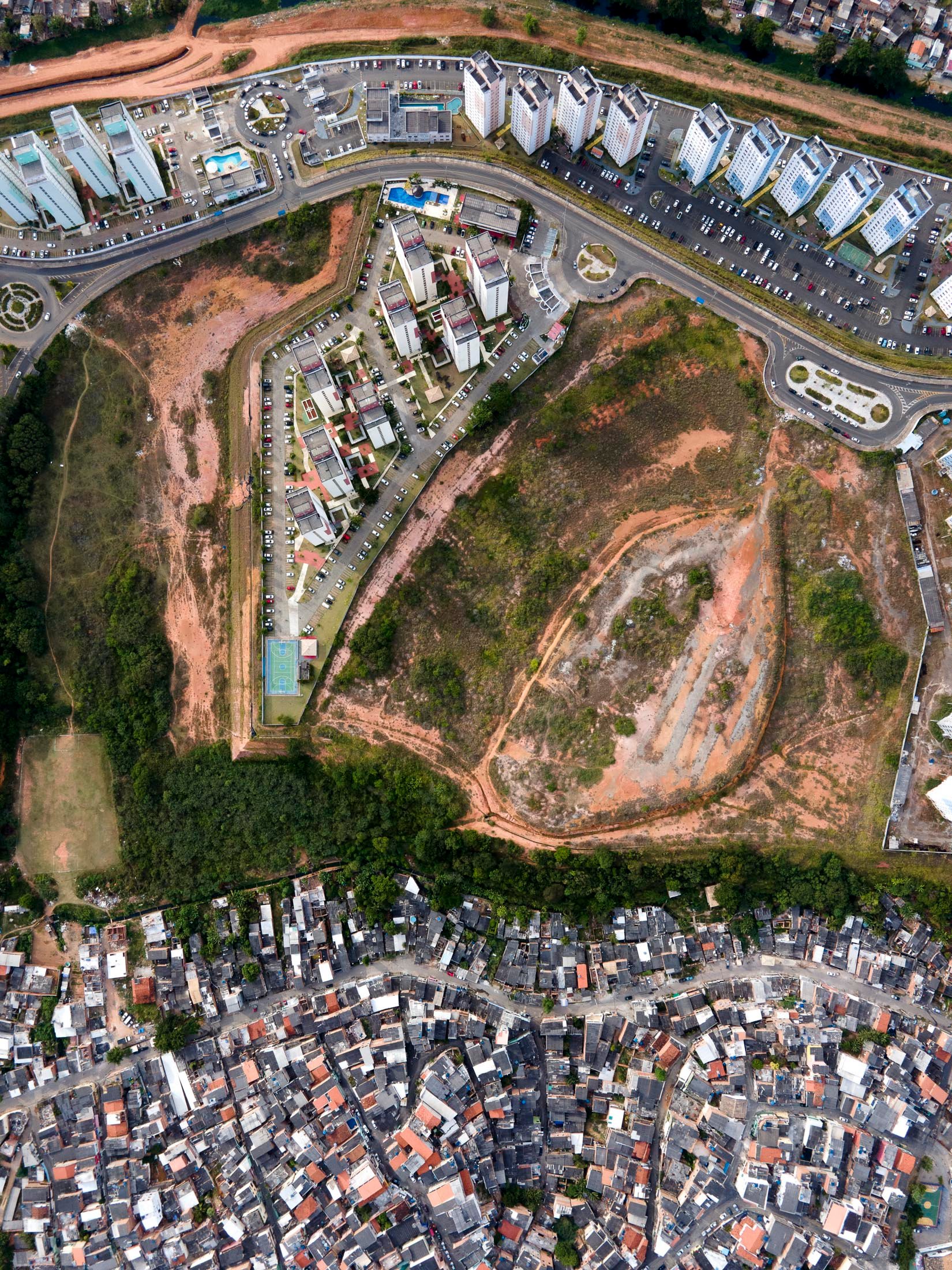 Divided urban fabric in Salvador, Bahia, where informal settlements border a modern gated community on a red dirt escarpment.