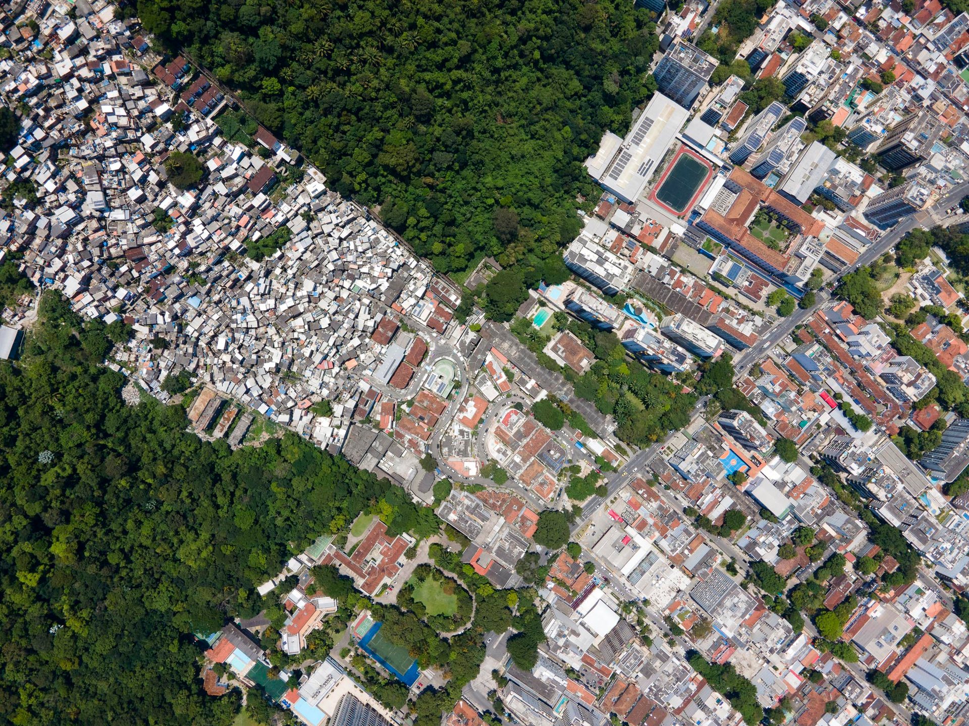 Overhead view of Santa Marta favela in Rio de Janeiro, densely packed on a forested hillside next to formal neighborhoods.