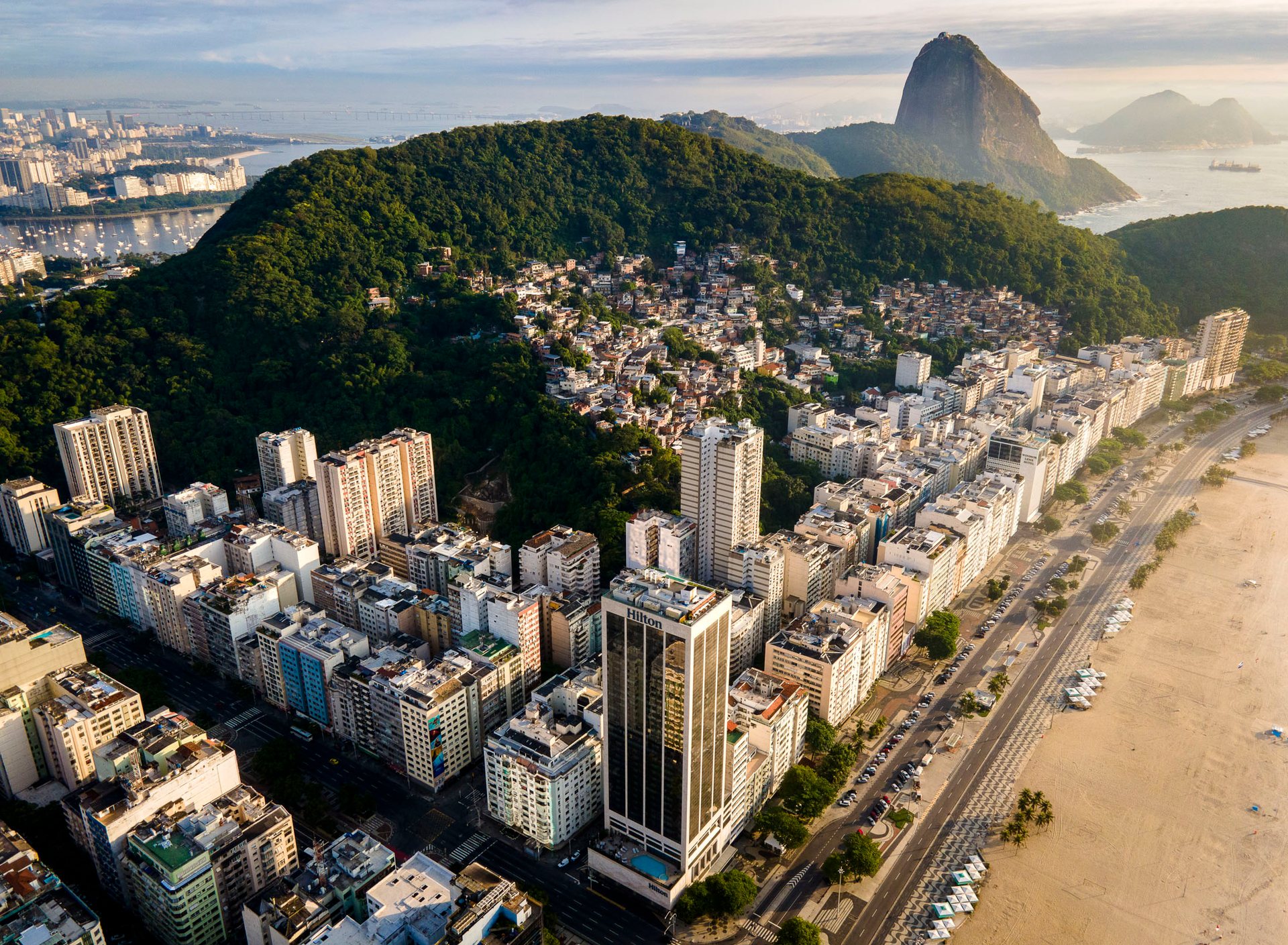 Leme Beach in Rio de Janeiro where high-rise beachfront apartments border favela settlements on the forested hill above.