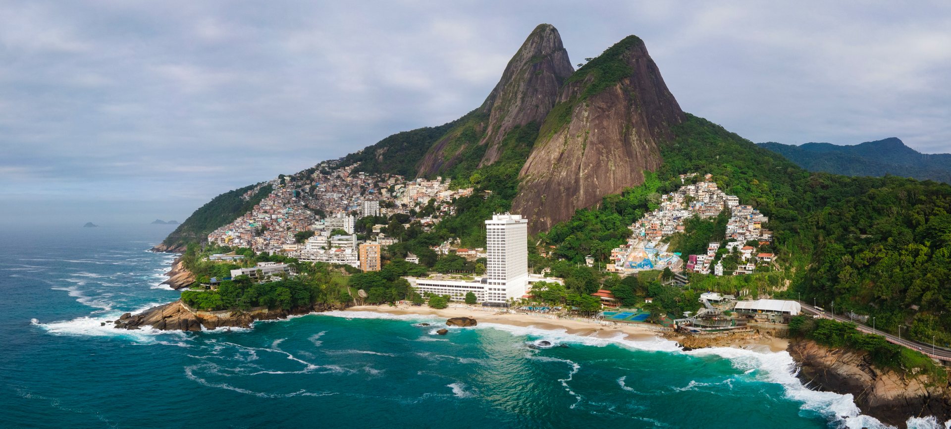Aerial view of Vidigal favela surrounding a luxury Sheraton hotel between twin coastal peaks in Rio de Janeiro, near Rocinha.