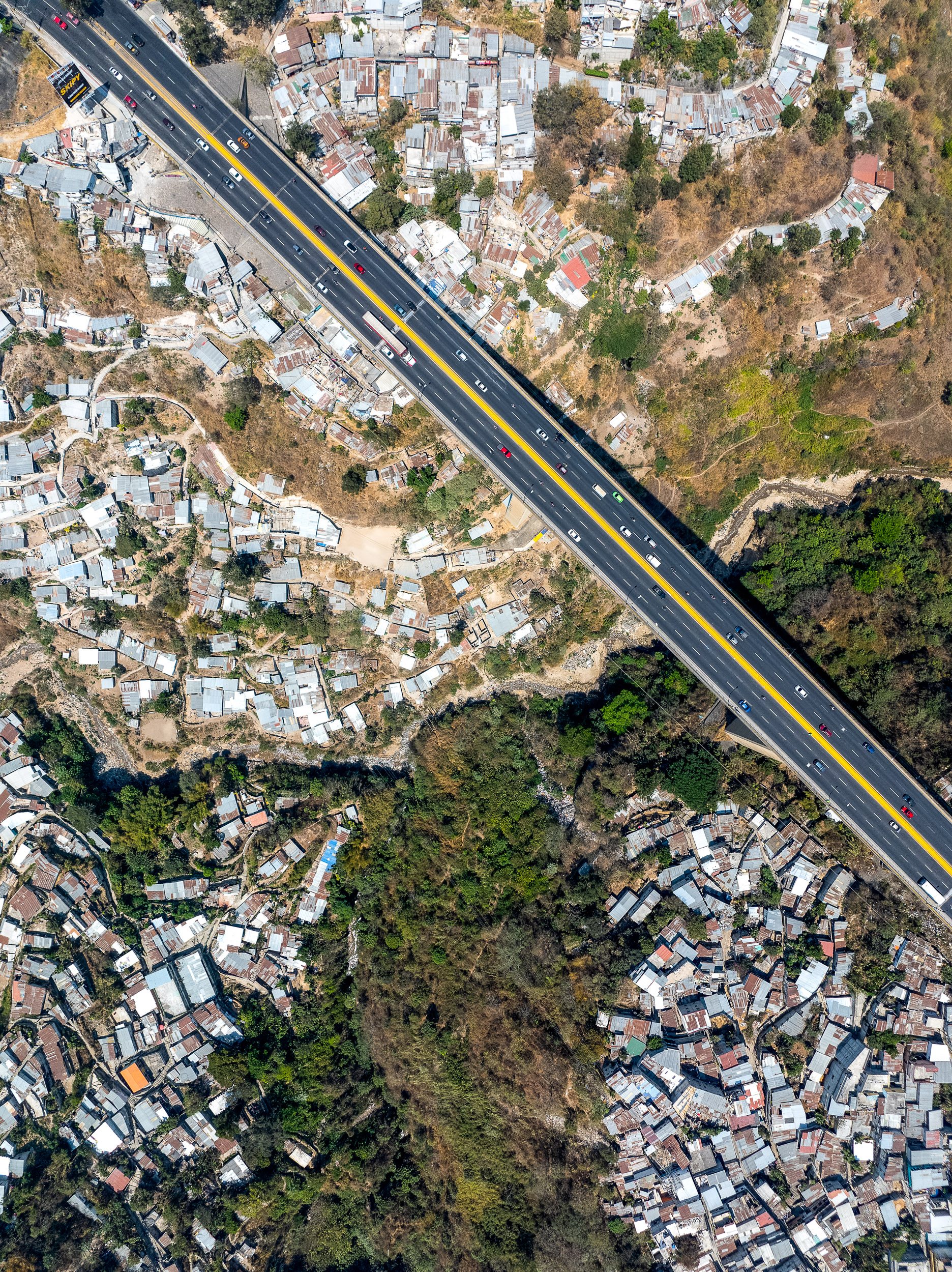 The city's main ring road passes above informal shacks which extend vertically down to the river's edge, and are essentially impossible to service or access, except by footpath.