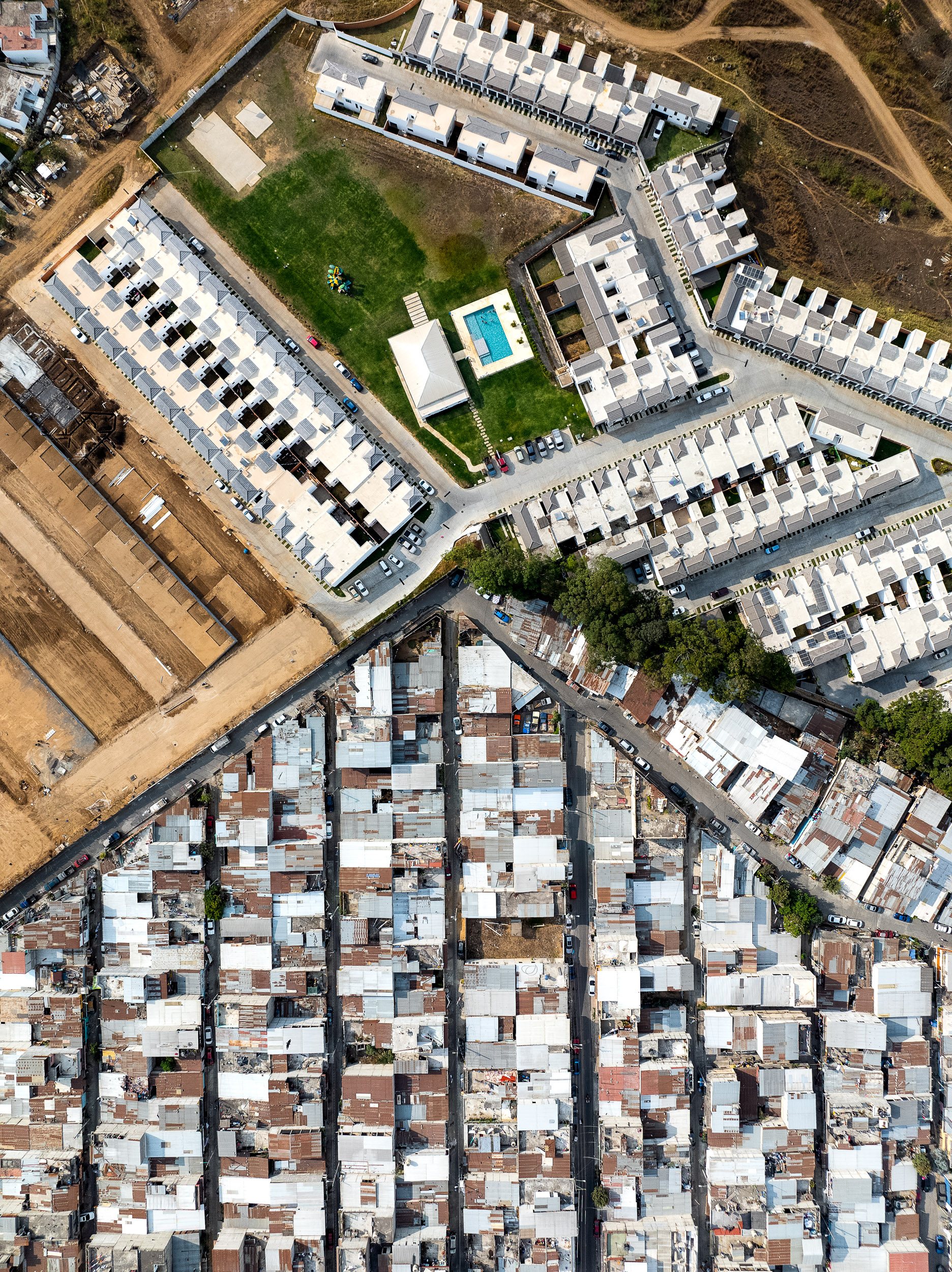 In Villa Nueva, on the southern edge of Guatemala City, a planned gated development, Ciudad Santa Clara, lays out its housing in a tight, repeating grid behind walls and guarded gates.