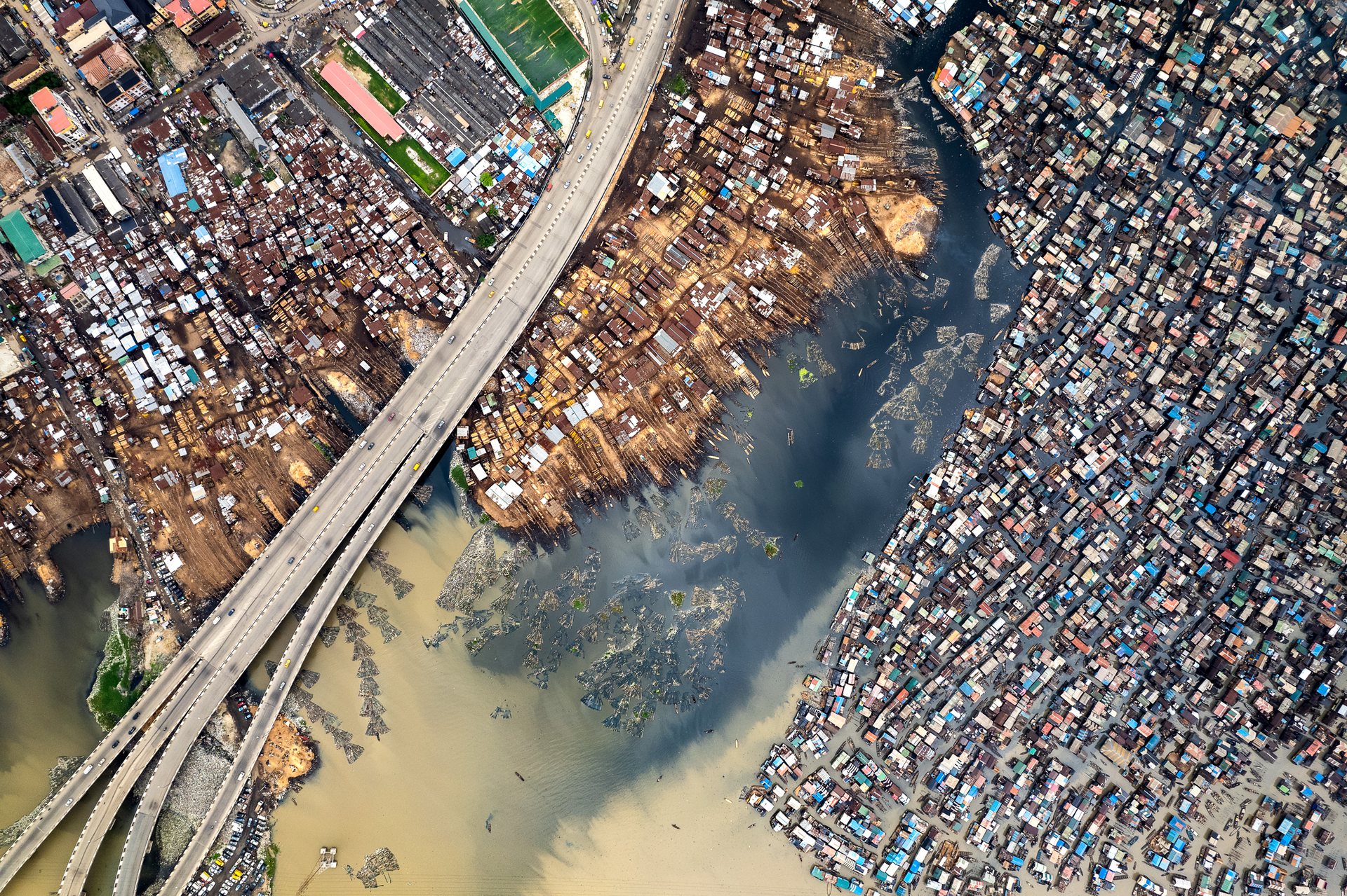Makoko spreads across the Lagos Lagoon near the Third Mainland Bridge, one of the longest bridges in Africa, which carries traffic high above a settlement most of those drivers will never enter.
