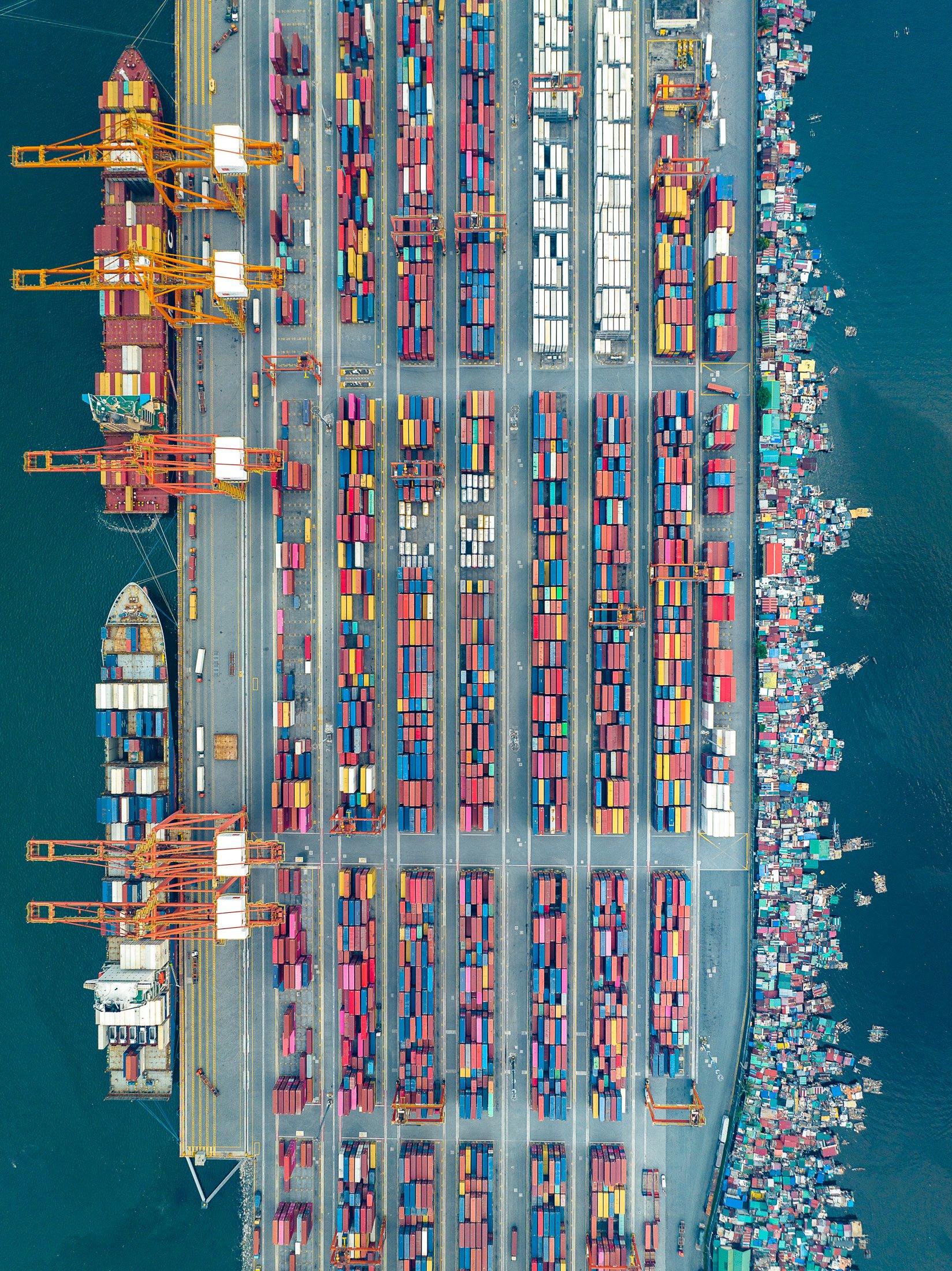 Aerial view of the Port of Manila, Philippines, showing neatly arranged shipping containers alongside floating informal settlements, highlighting inequality in urban logistics zones.