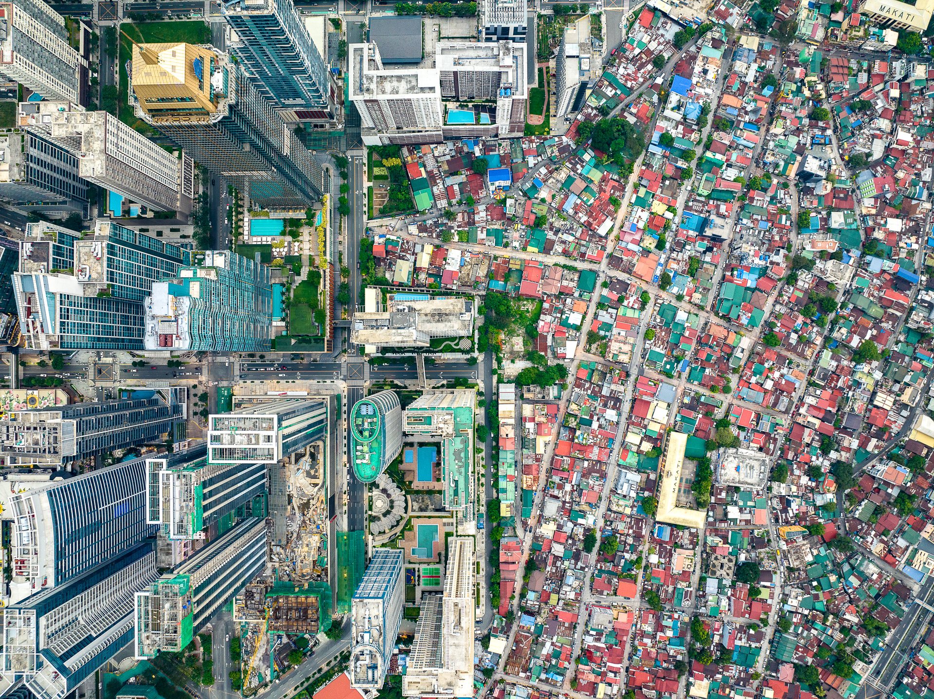 Drone view of Manila showing gleaming skyscrapers of Bonifacio Global City (BGC) standing in stark contrast to the adjacent lower-income South Cembo neighborhood with compact housing.