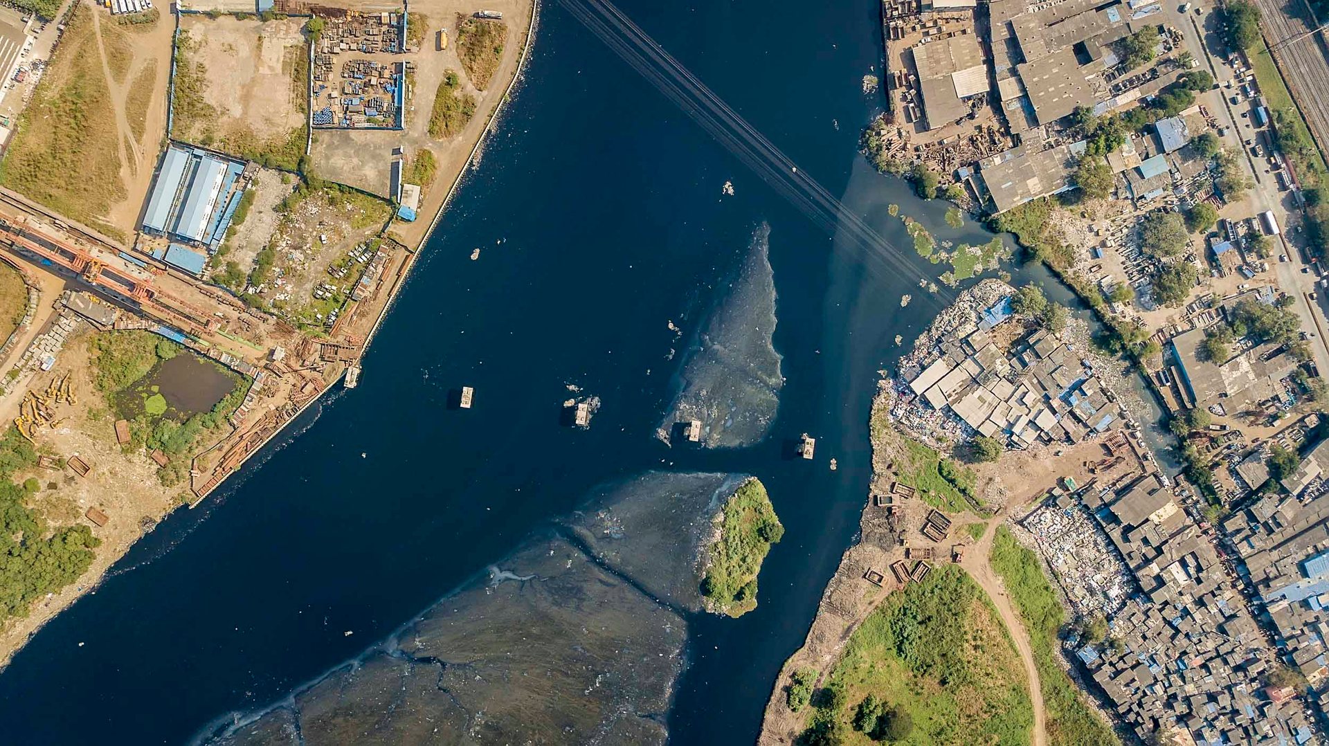 Overhead image showing stark contrast between luxury towers and blue-roofed slums divided by a narrow waterway.