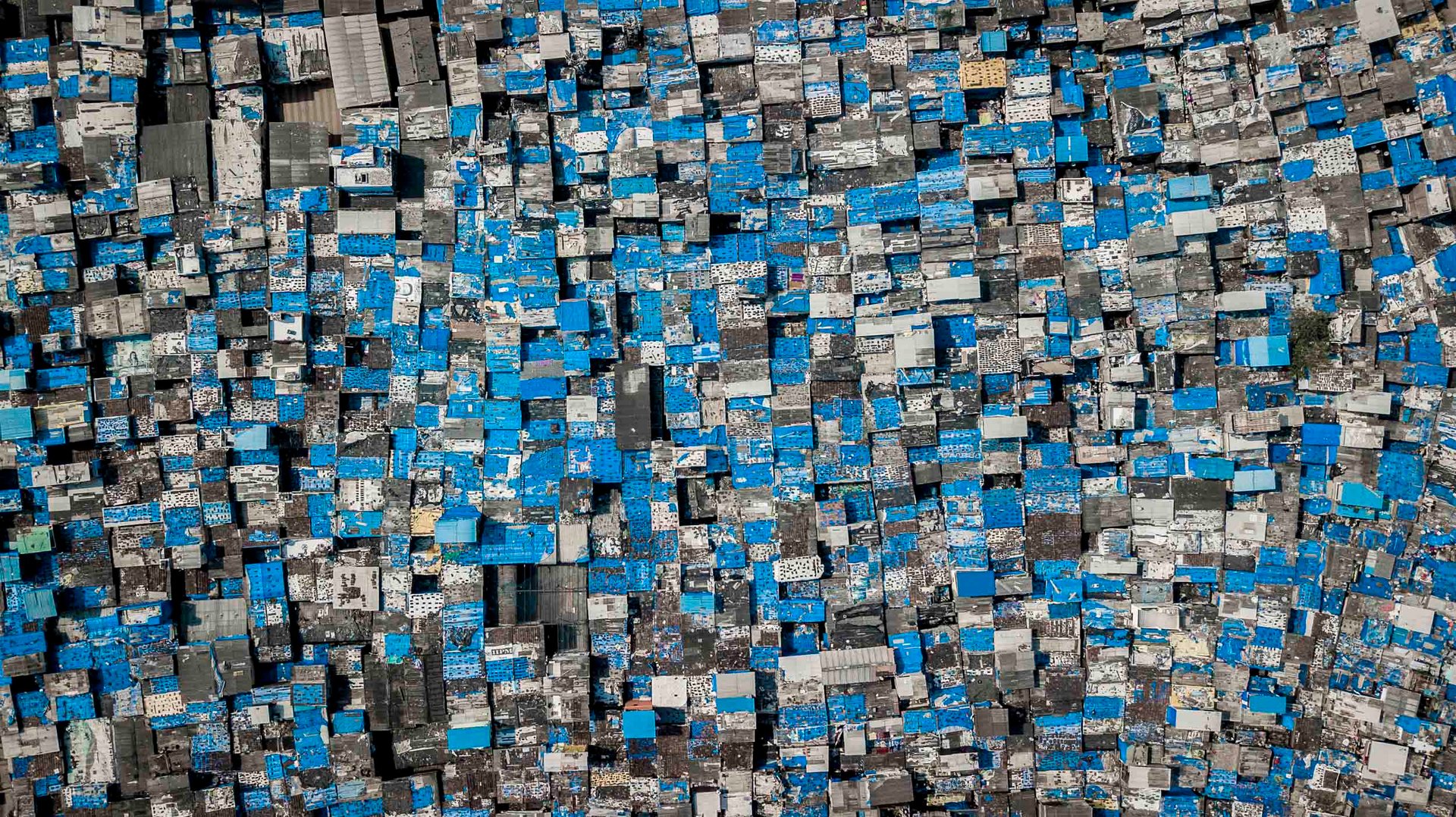 Tightly packed grid of blue-roofed dwellings in northern Mumbai showing high density of informal housing.