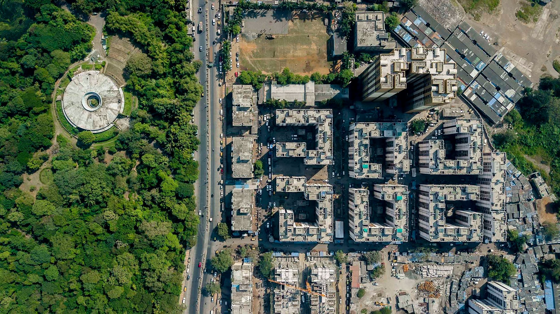 Circular park near the Malad Mangrove Park bordered by modern residential towers and undeveloped land.