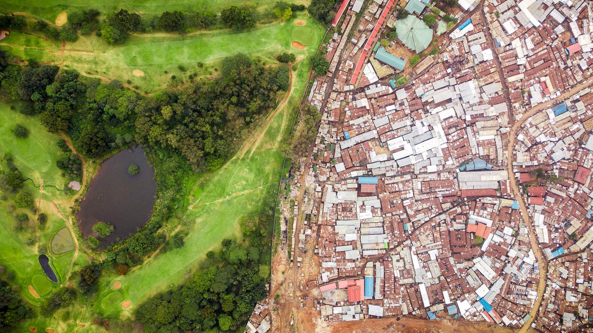 Aerial view of Kibera slum bordering a lush urban golf course in Nairobi, Kenya.