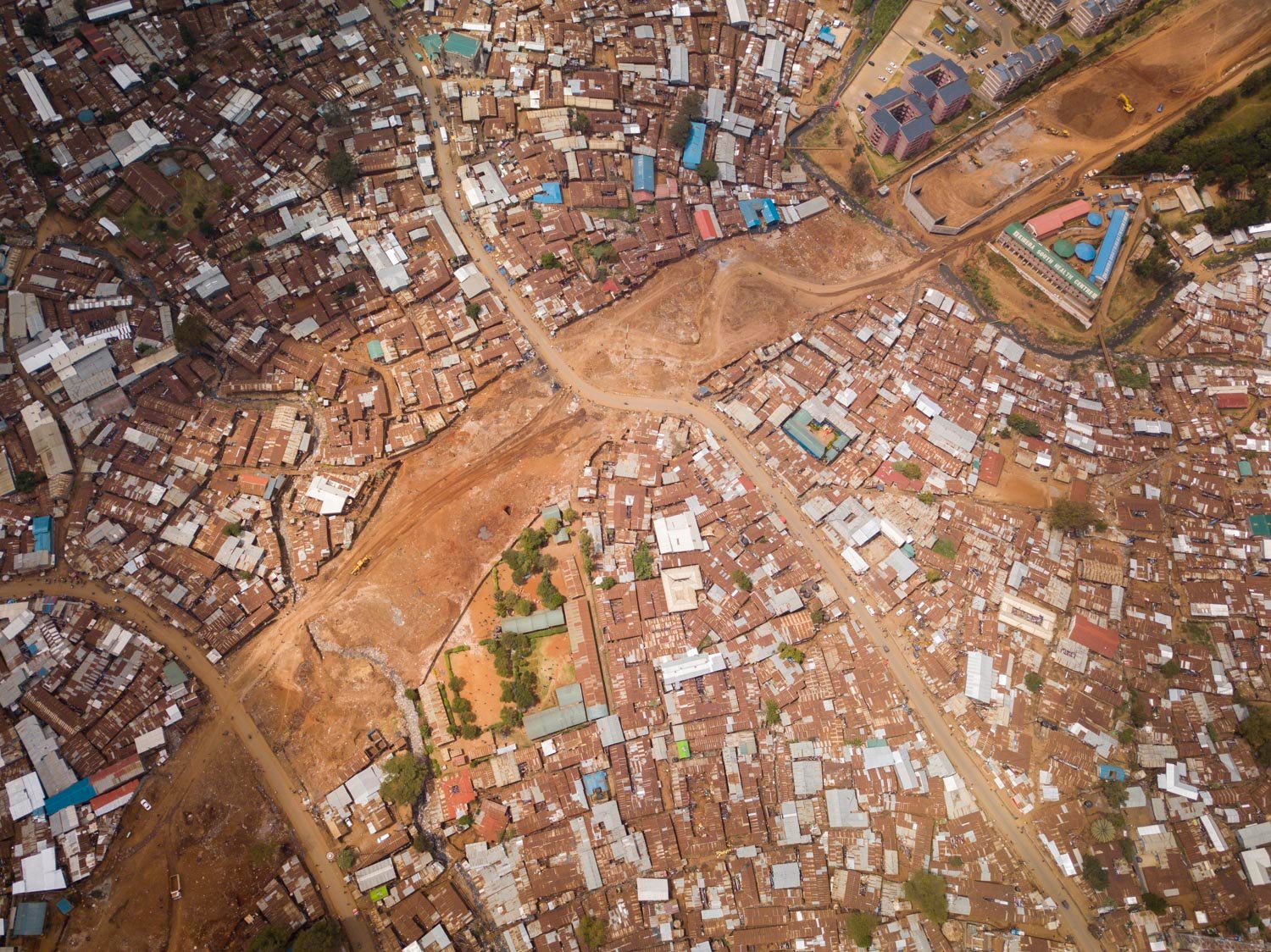 Aerial image of Nairobi informal settlement with reddish soil roads and crowded tin-roof structures in kibera.