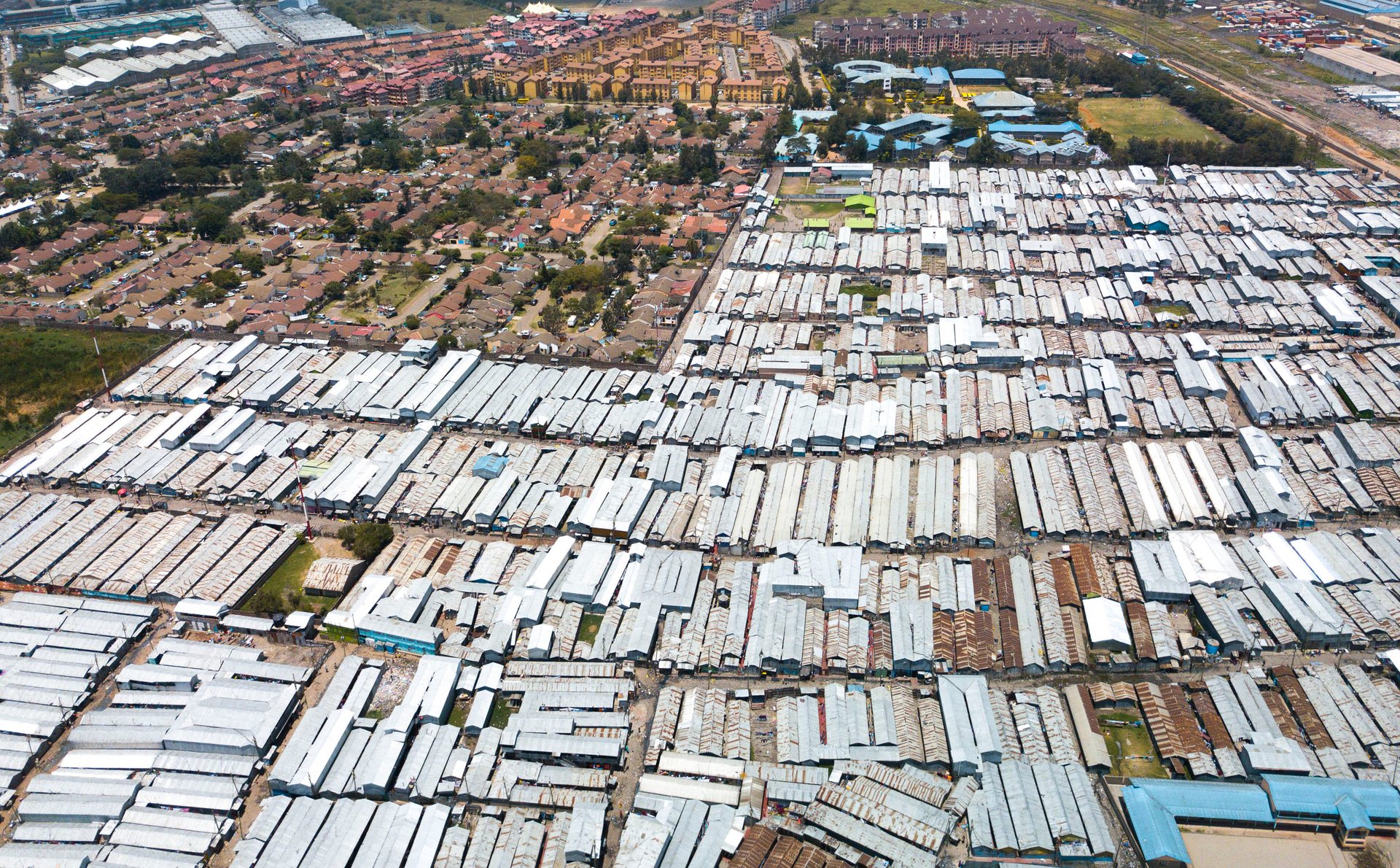Drone image of large rectangular market structures in Nairobi beside sprawling informal housing.