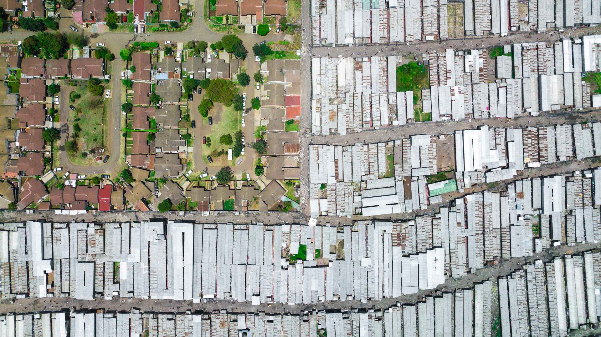 Drone view of contrast between informal densely packed tin-roof homes and an orderly planned housing grid in Mukuru.