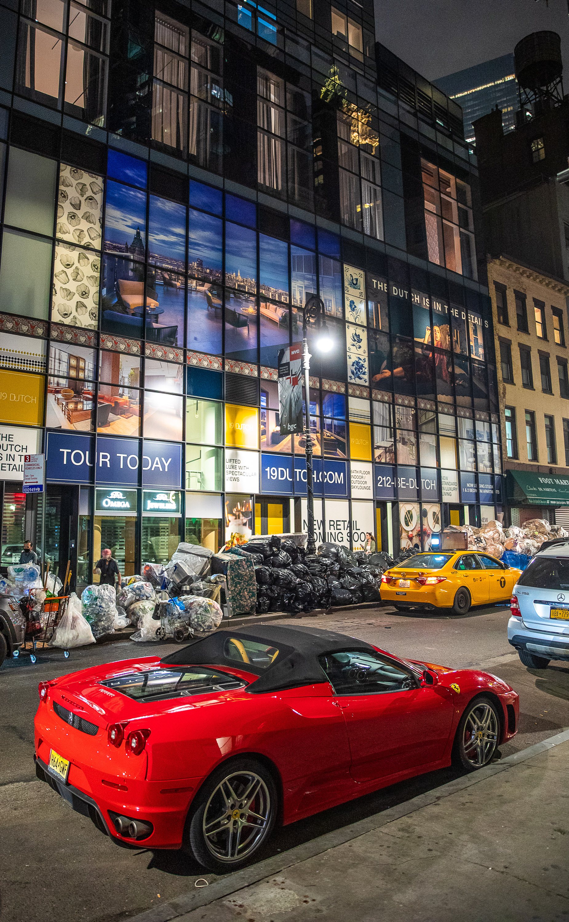 A Ferrari parked in front of a luxury building in the Financial District, while recyclers search for aluminum cans discarded in the mounds of trash nearby.