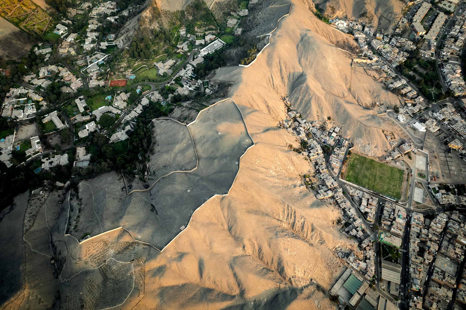Walls enclose green lawns and swimming pools in Lima, sometimes extending over hilltops in Las Casuarinas.