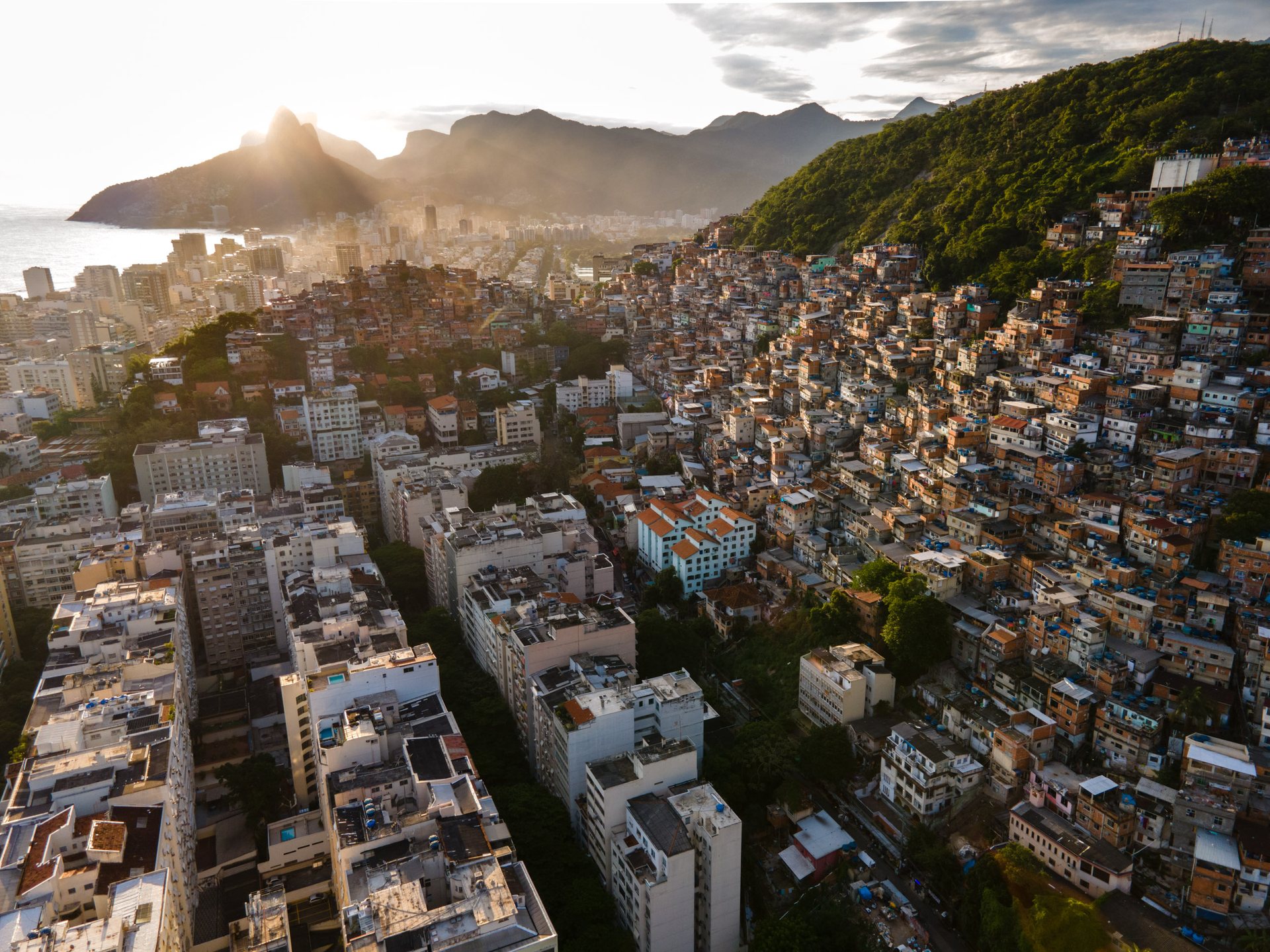 Aerial view of Cantagalo favela cascading down a hillside in Rio de Janeiro, juxtaposed with high-rise luxury apartments nearby.