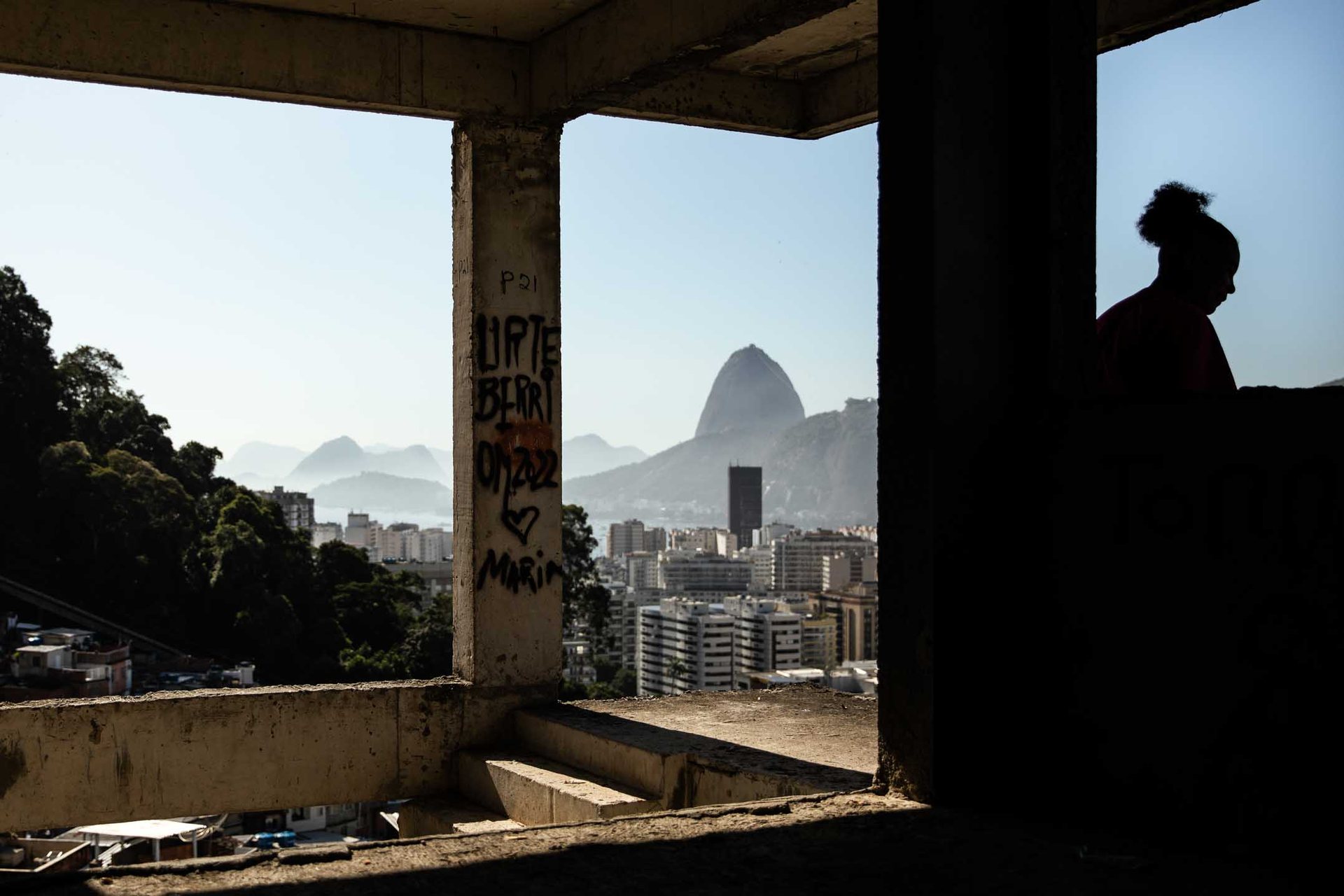A woman in silhouette in an abandoned building in Santa Marta favela with Sugarloaf mountain in the background.