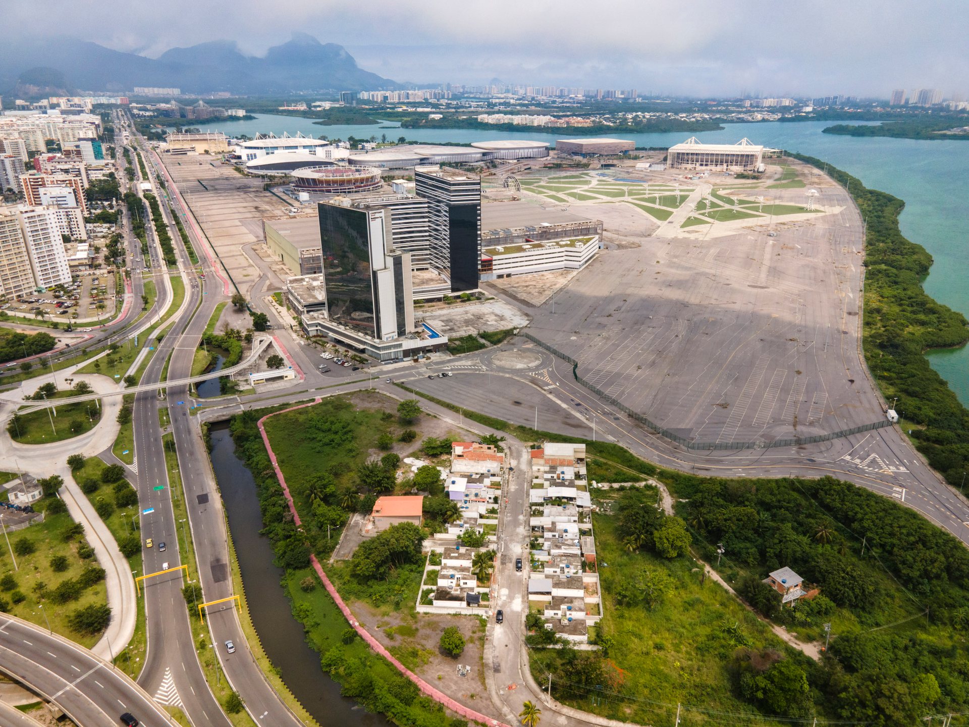 Aerial perspective of Rio’s Olympic redevelopment zone, with Vila Autódromo settlement visible beside wide highways and cleared land.