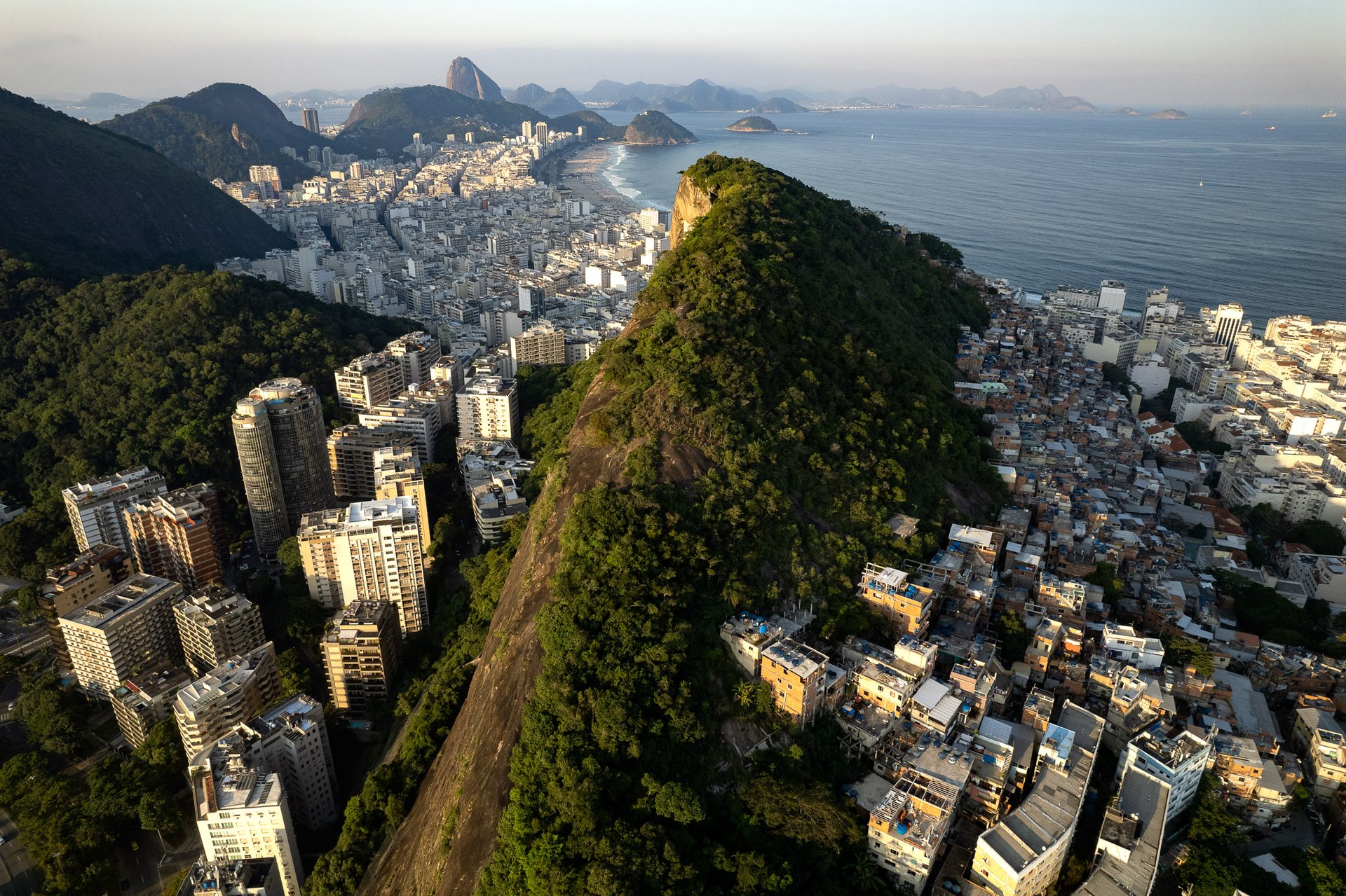 Aerial view of a forested ridge in Rio de Janeiro dividing high-rise apartment blocks from dense favela housing, illustrating the role of topography in shaping urban segregation.