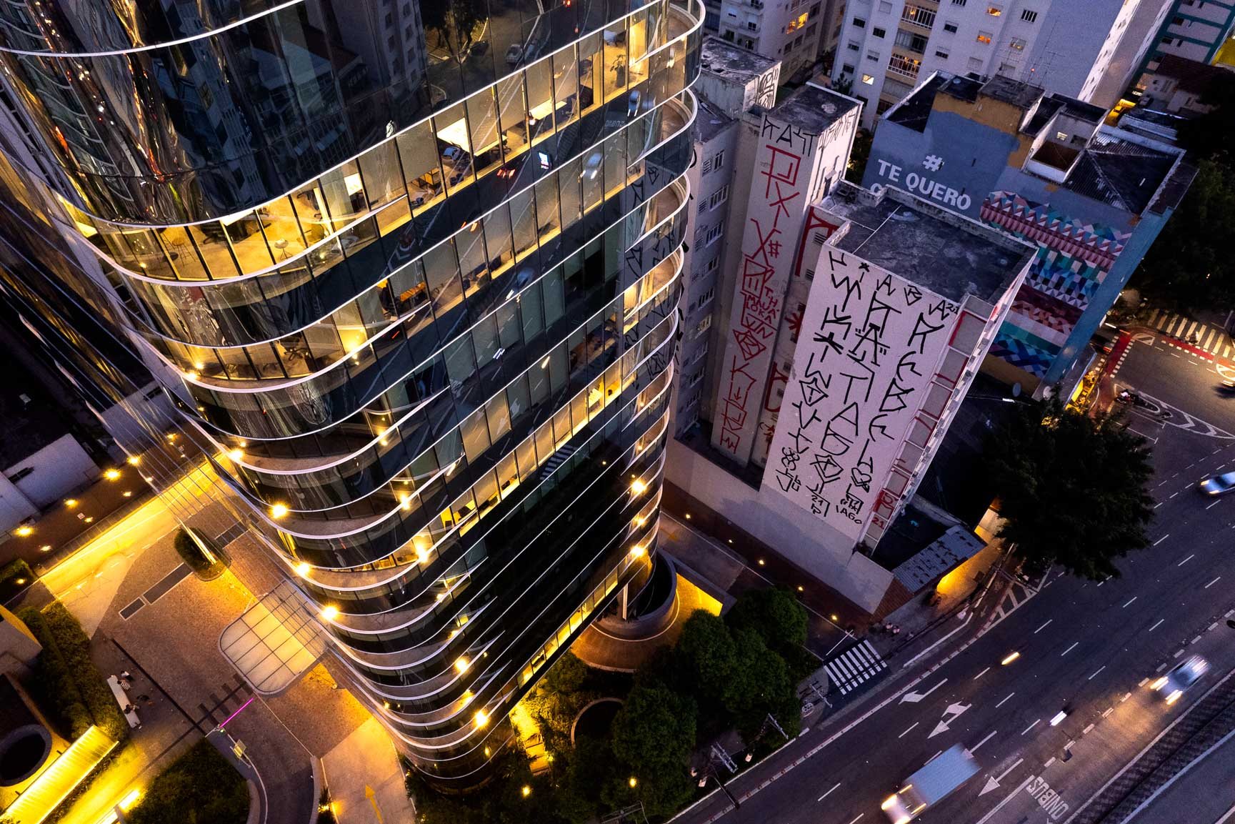 Side-by-side buildings in São Paulo—one modern with curved glass, the other a weathered concrete structure.