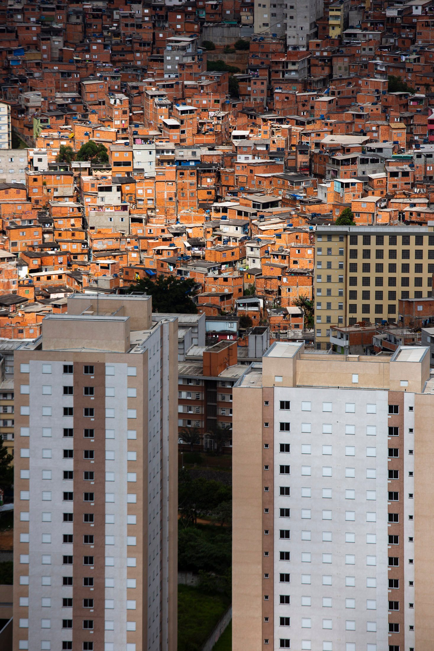 Close-up aerial view of a São Paulo favela with stacked red-brick homes rising against newer apartment blocks, illustrating vertical density and inequality.