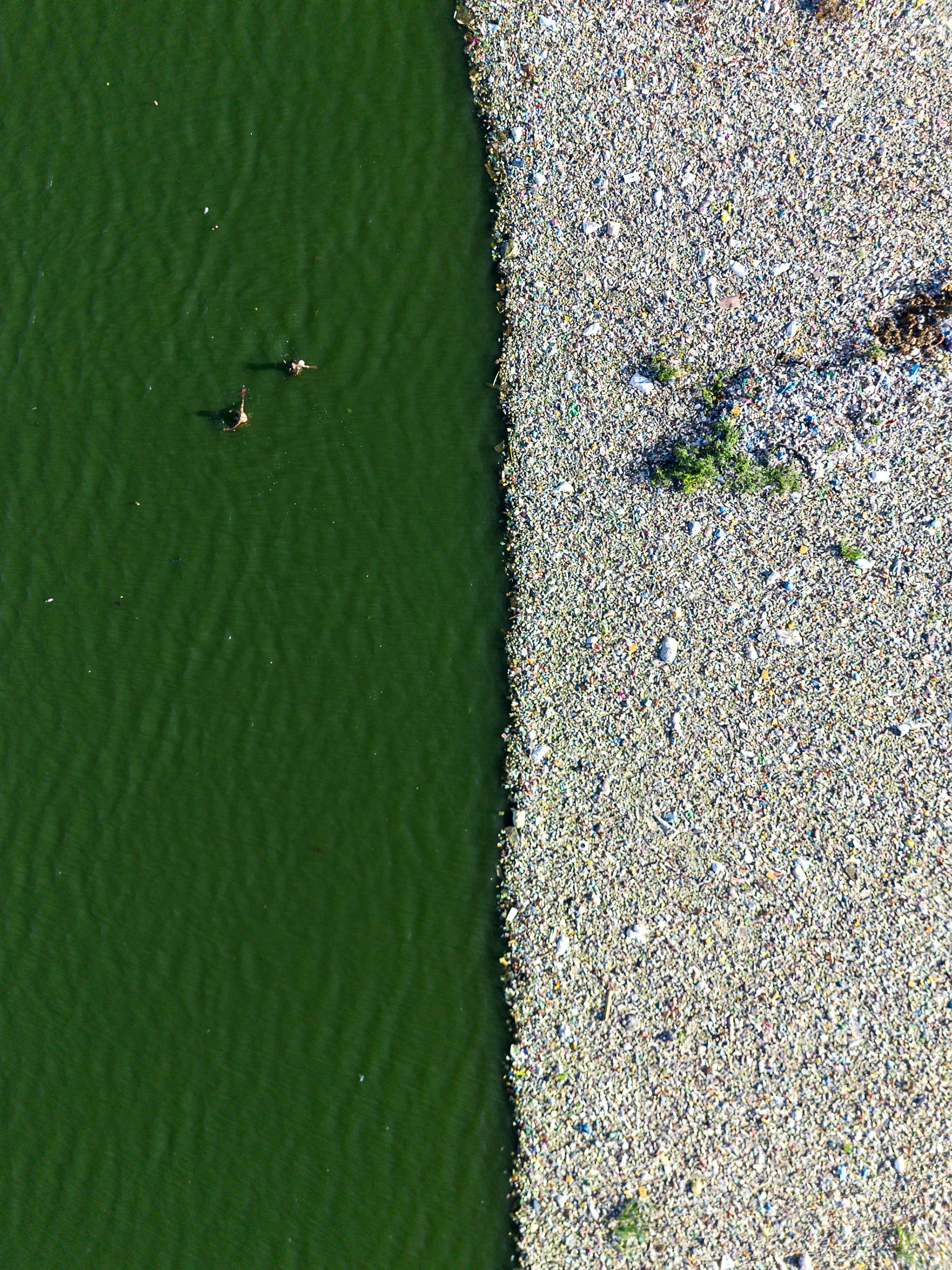 Two men adjust their fishing net next to a huge floating garbage patch, in Msisi, central Lusaka.